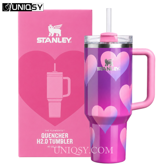 Stanley Quencher H2.0 tumbler in a pink and purple heart pattern, shown next to its pink retail box on a white background.