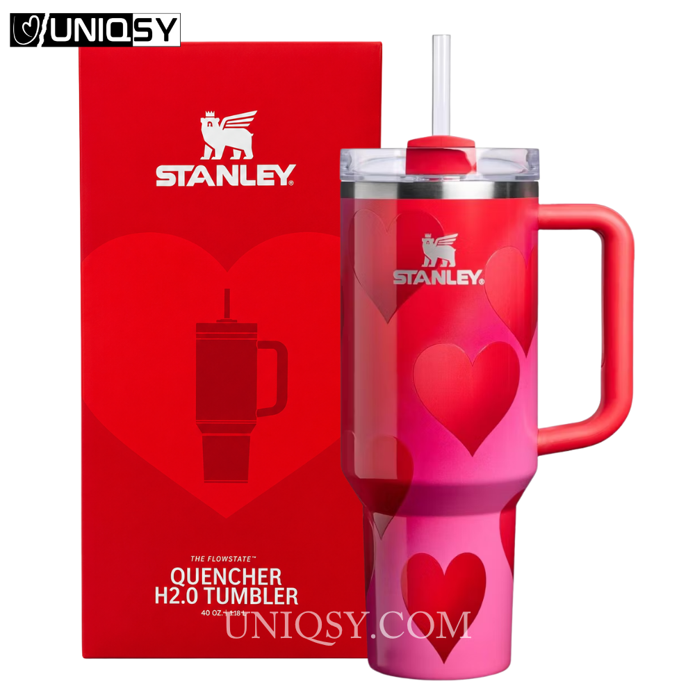 Stanley Quencher H2.0 tumbler in a pink gradient finish with heart patterns, shown next to its red packaging box on a white background.