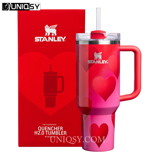 Stanley Quencher H2.0 tumbler in a pink gradient finish with heart patterns, shown next to its red packaging box on a white background.